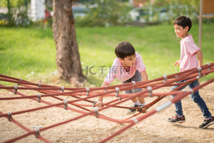 小亚洲男孩爬上绳子在公园里