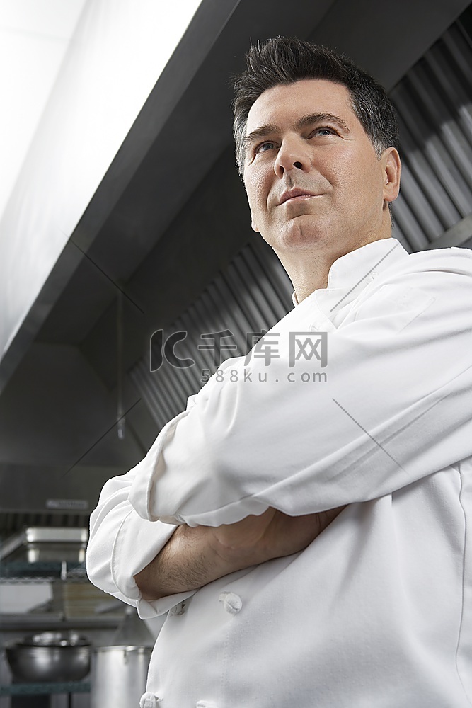 厨房里双臂交叉的男厨师，低角度