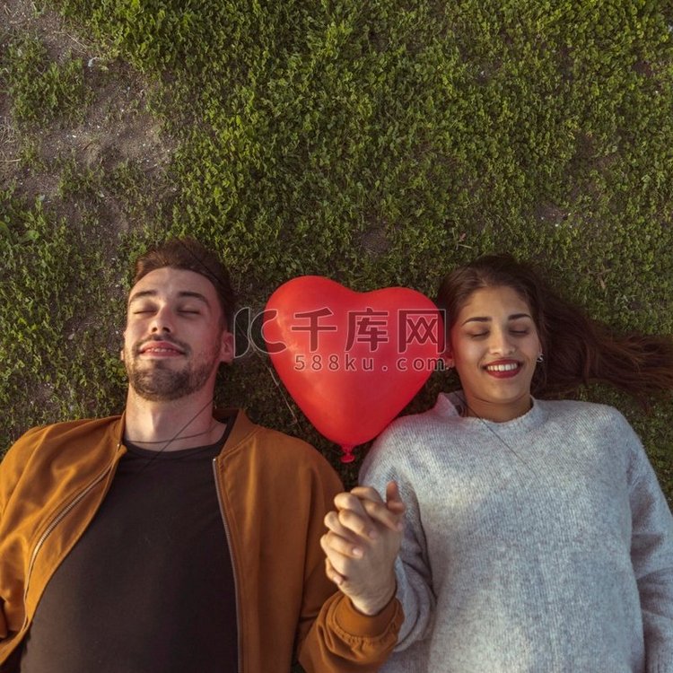 年轻夫妇躺在草地与心脏气球