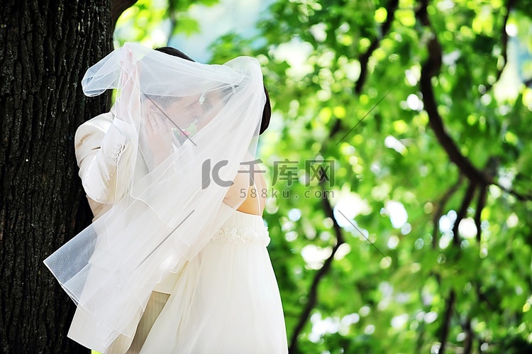 身着白色礼服的新郎和新娘在绿树