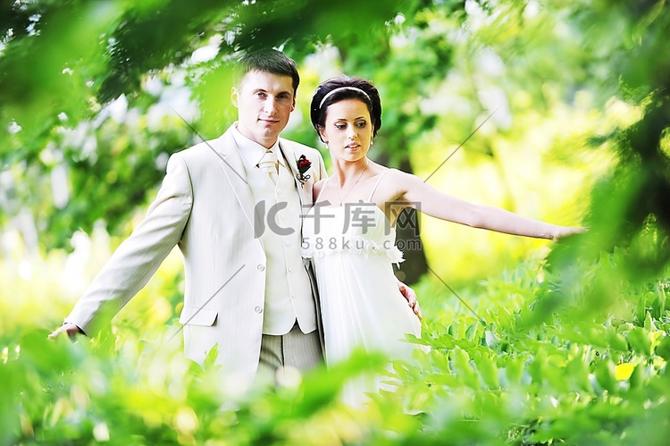 身着白色礼服的新郎和新娘在绿树