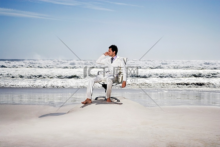 一位年轻的商人坐在海滩的办公椅