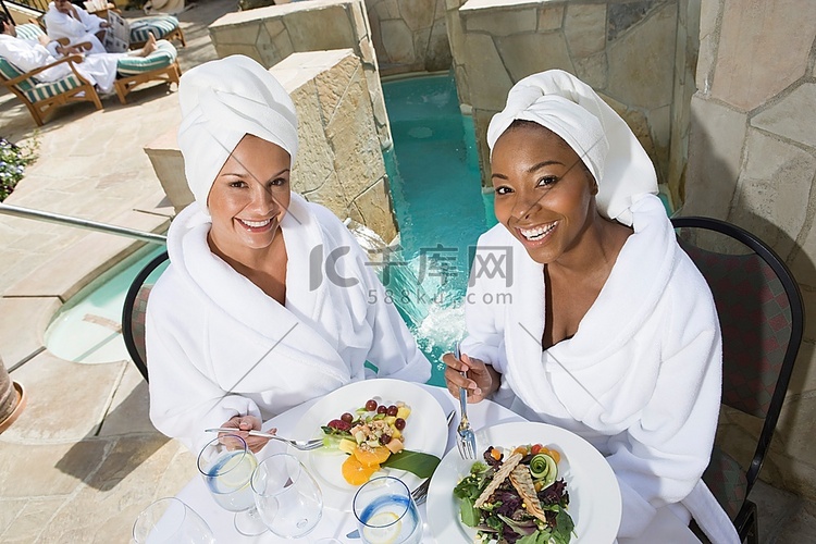 身着浴袍的妇女在游泳池边吃饭的