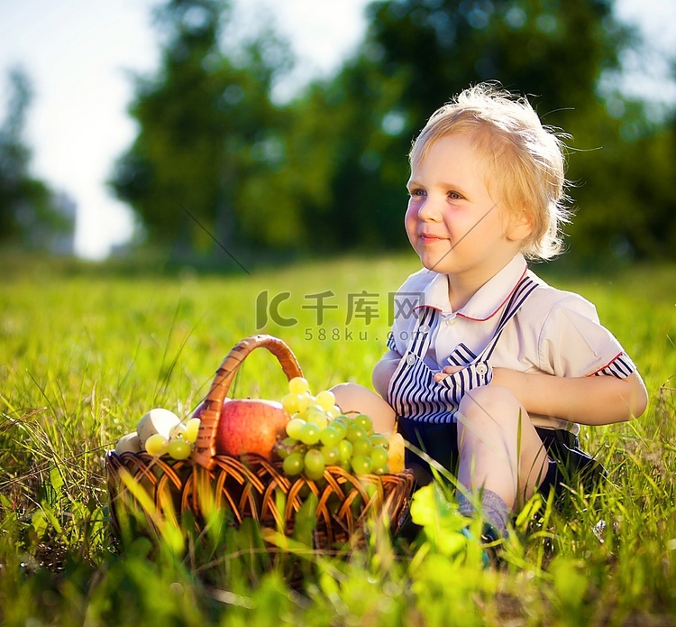 小男孩提着一篮子水果坐在草地上