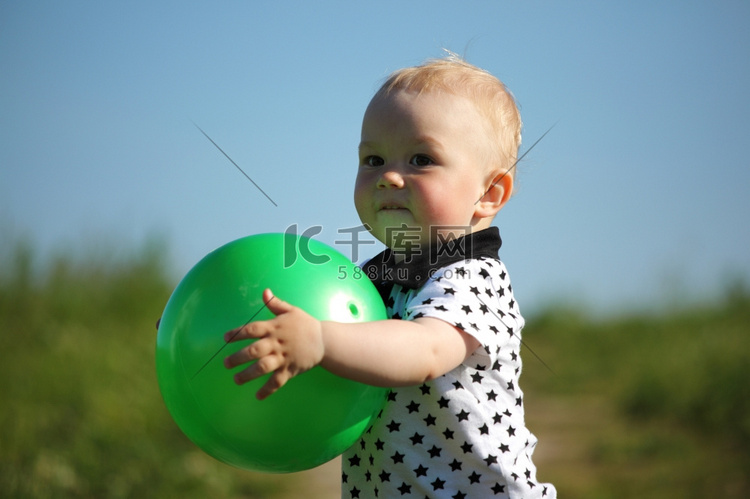 小男孩玩在绿草与绿色球