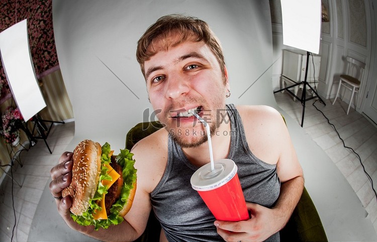坐在扶手椅上吃汉堡包的胖子