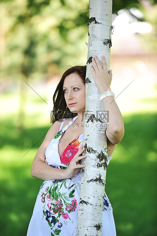 美丽的未来妈妈站在树旁。夏日与