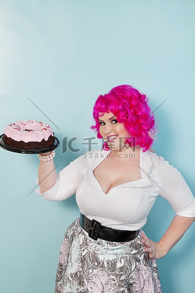 画像的年轻女子站在臀部手拿蛋糕