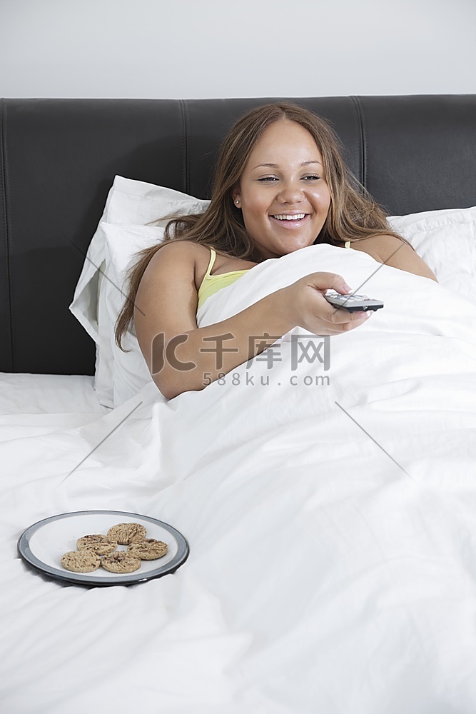 快乐的年轻女人在家躺在床上看电