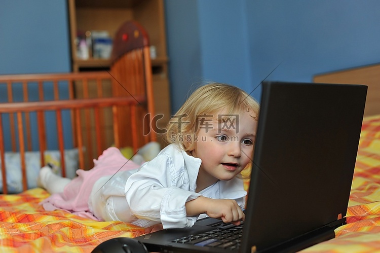 漂亮的小女孩拿着笔记本电脑躺在
