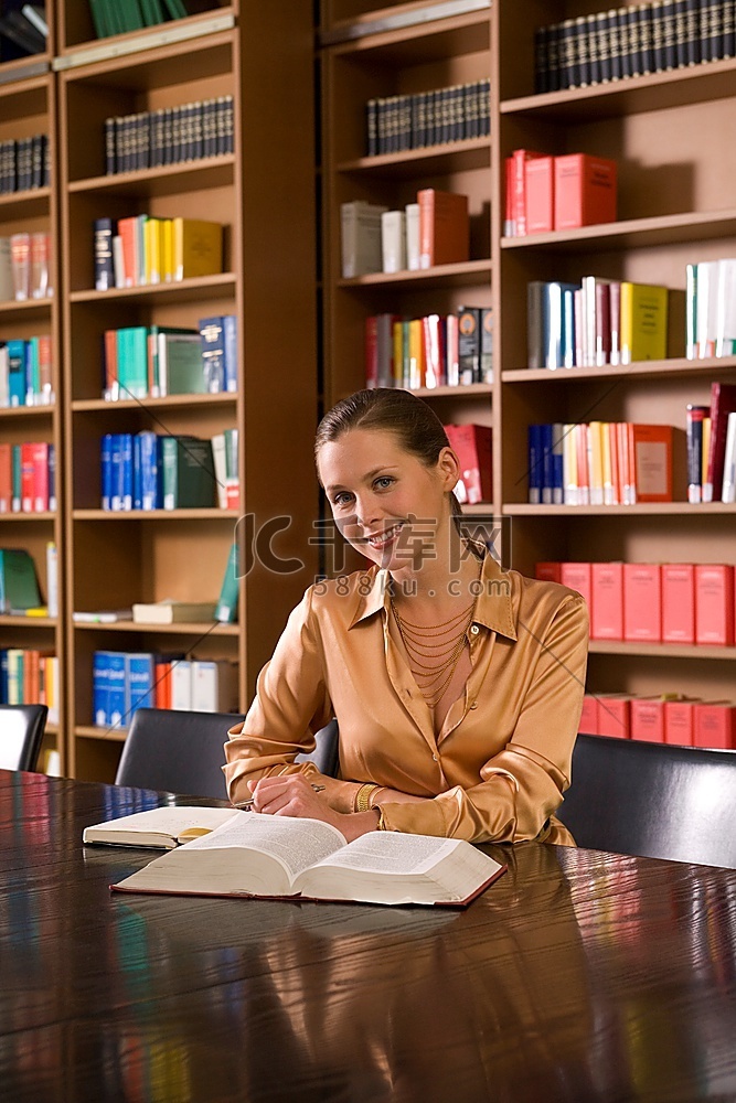 图书馆书桌前拿着书的年轻女子，