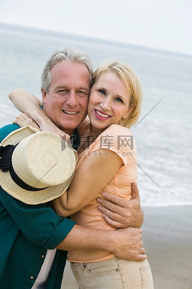 中年夫妇拥抱在海滩和看照相机