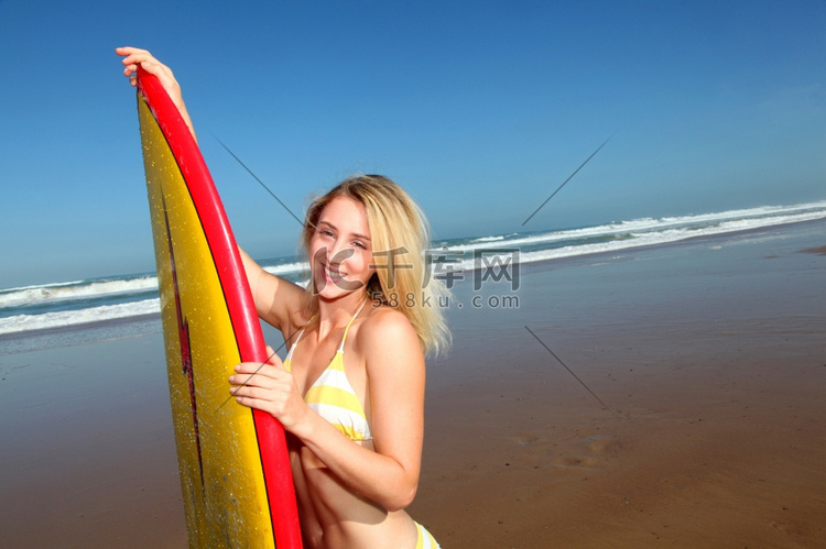 美丽的金发女子拿着冲浪板站着