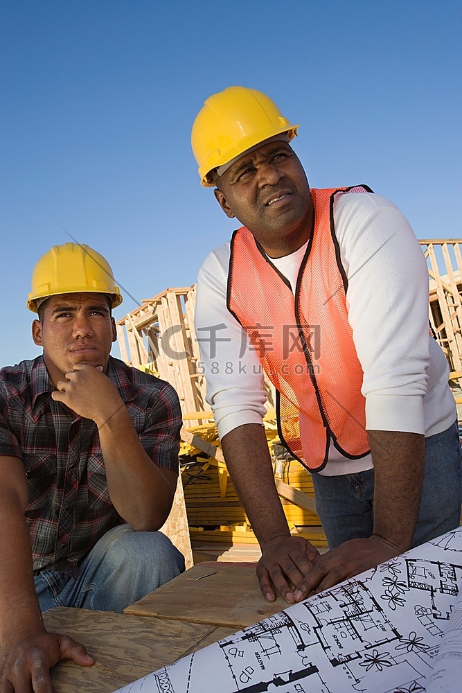两名建筑工人靠在桌子上，手里拿