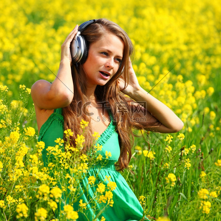 戴着耳机的年轻女子在油籽花田里