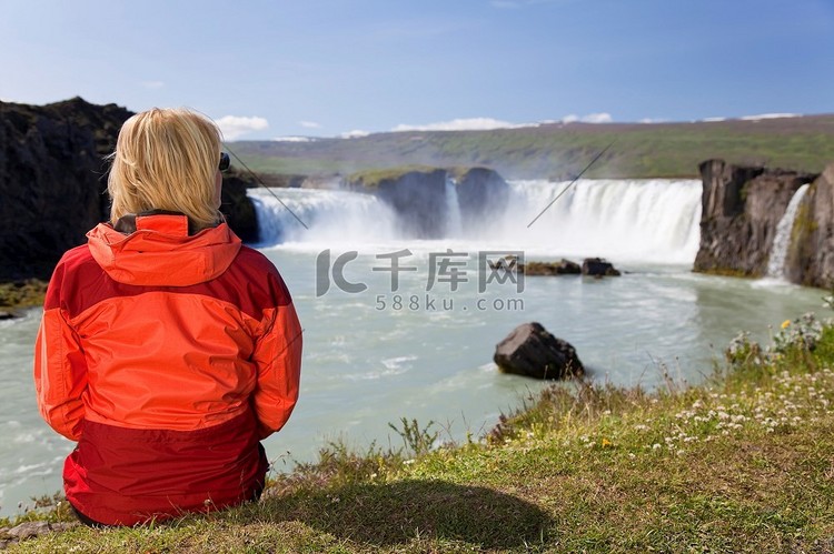 一位年轻女子坐在那里看着瀑布。