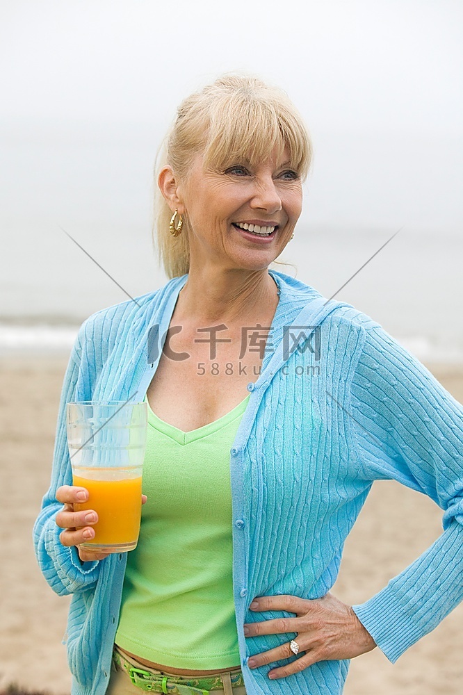 海滩上的中年妇女手里拿着一杯橙