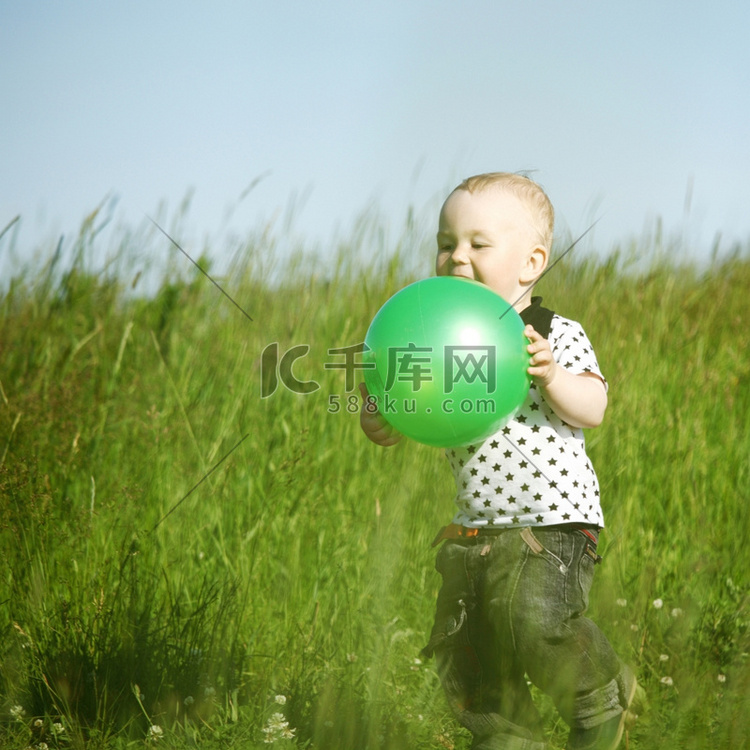 小男孩拿着绿球在绿草地上玩耍
