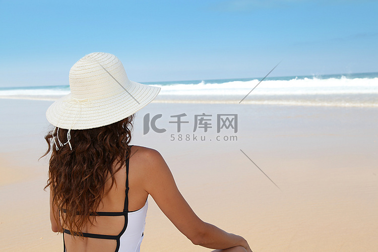 戴着草帽坐在海滩上的美女