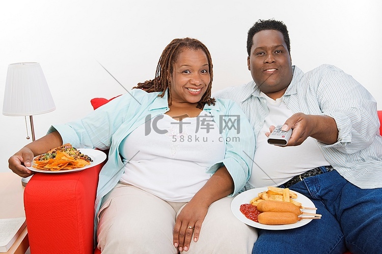 中年人超重夫妇坐在沙发上吃饭和
