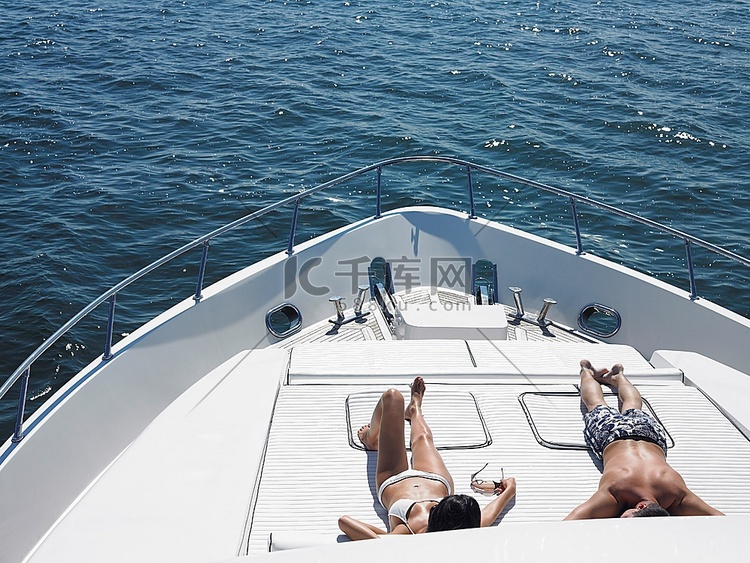 年轻夫妇在海上游艇首晒日光浴俯