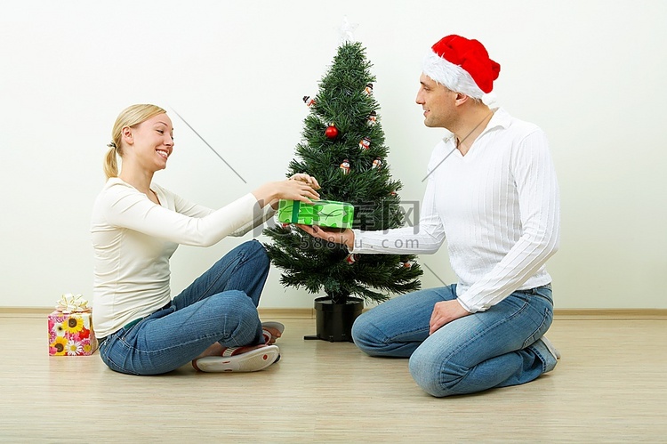 男人靠着一棵圣诞松树给女人一份