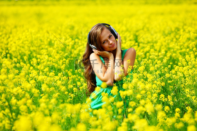 戴着耳机的年轻女子在油籽花田里
