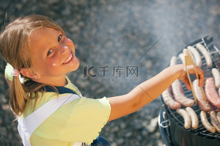 小女孩用烧烤架准备肉类和香肠