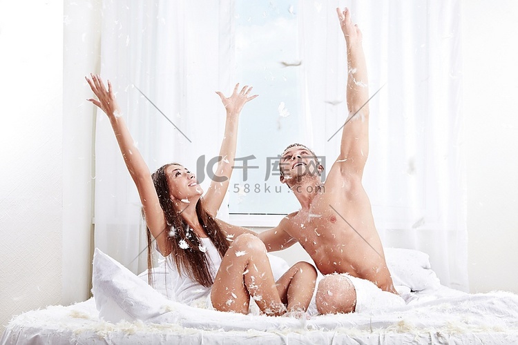 一对微笑的年轻夫妇在床上抓羽毛
