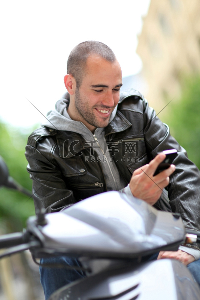 坐在摩托车上的年轻人拿着电话