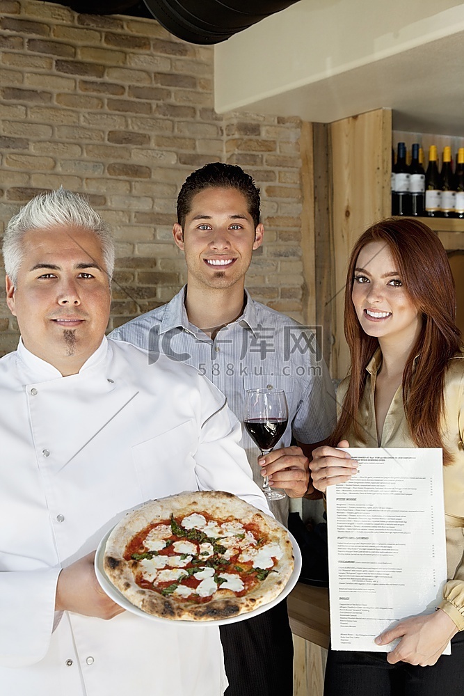 快乐厨师与年轻夫妇手持披萨的合