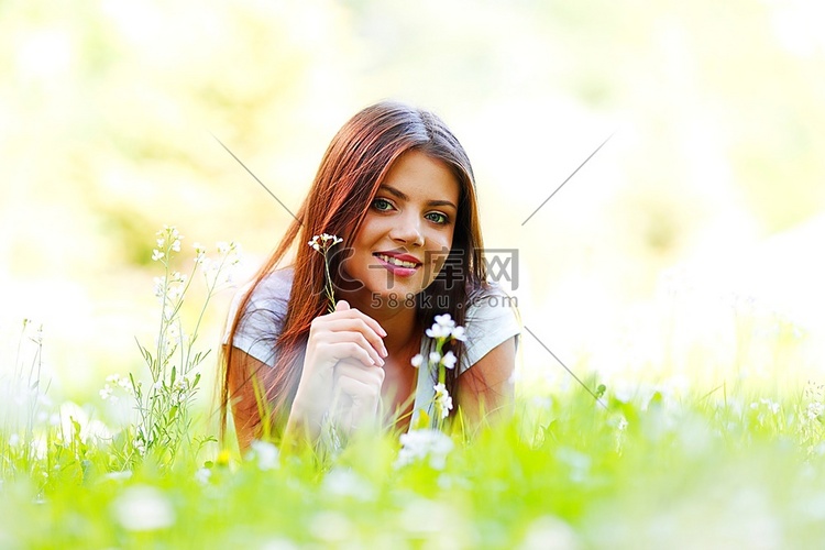 美丽的年轻女子躺在花丛中的草地
