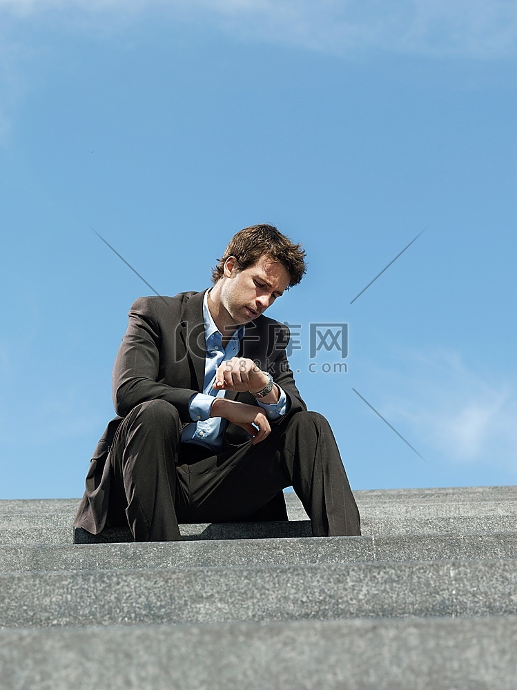 一名商人坐在户外的台阶上看手表