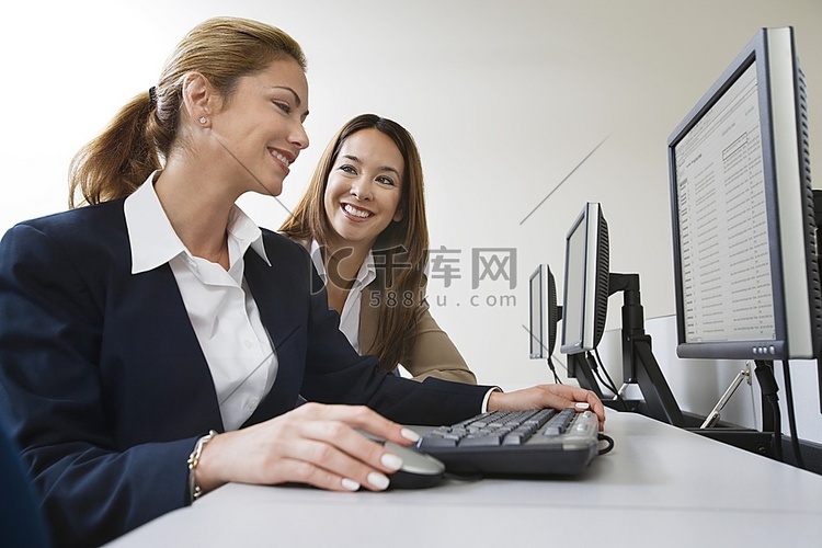 两位女商人对着桌上的电脑微笑