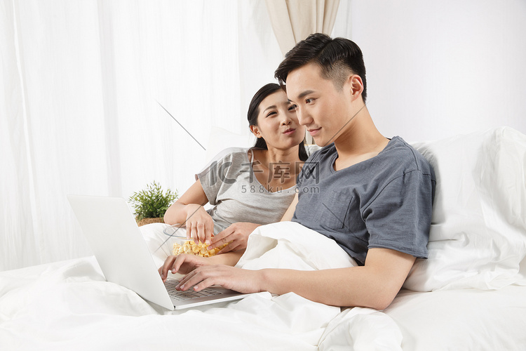 青年情侣坐着床上看电脑