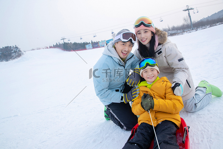 滑雪场上父母和坐在雪上滑板的儿