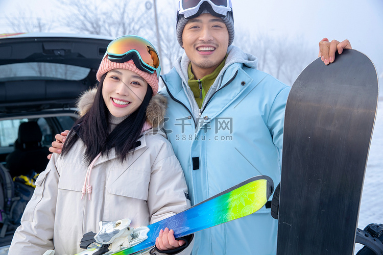 快乐的青年伴侣拿着滑雪板靠在一