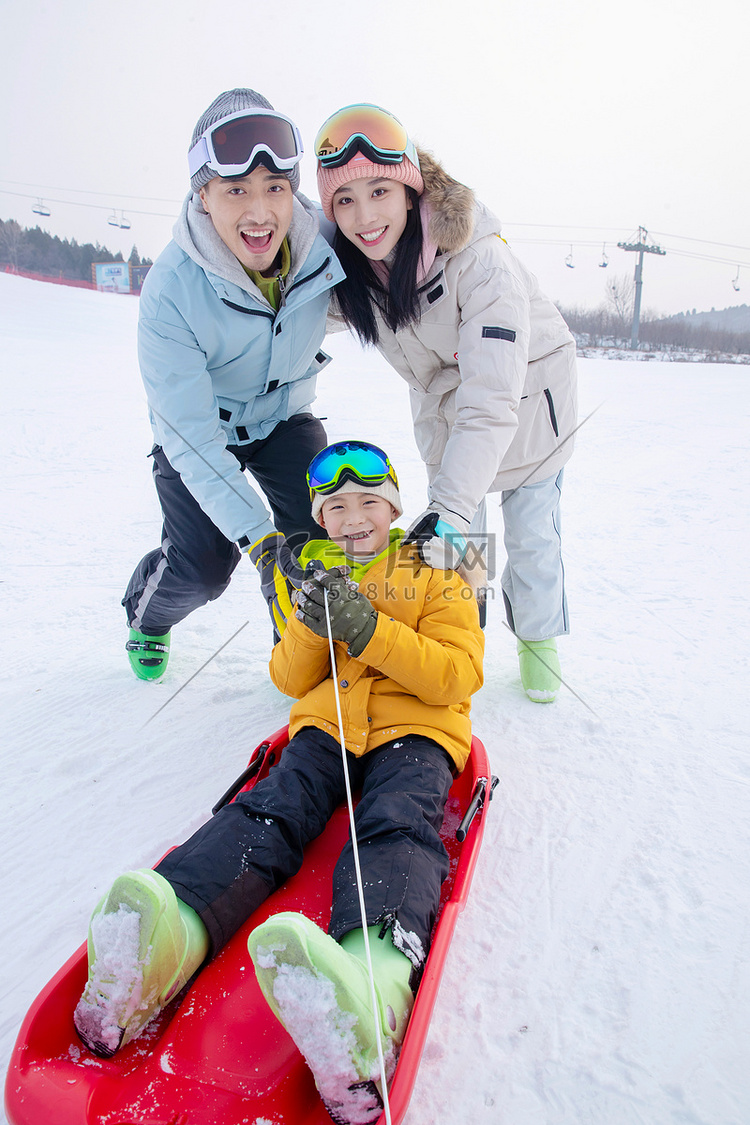 滑雪场上父母推着坐在雪上滑板的