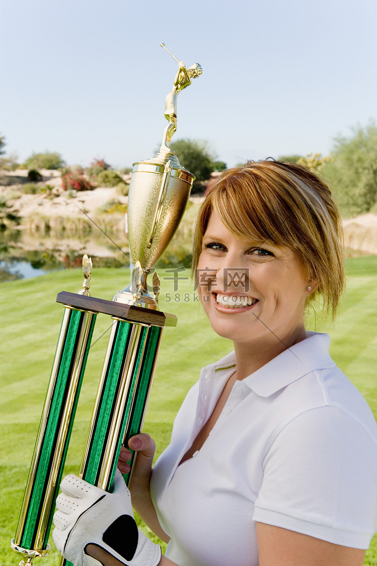 在高尔夫球场上拿着奖杯的快乐女