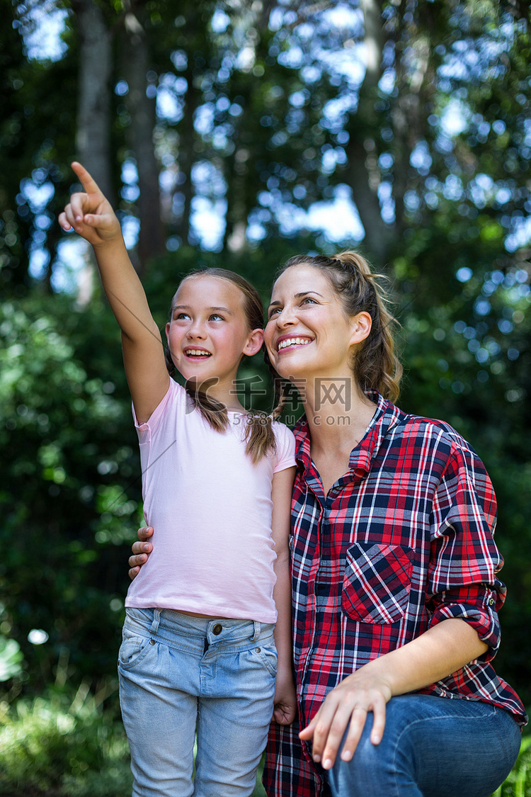 快乐的女孩站在妈妈身边时向上指