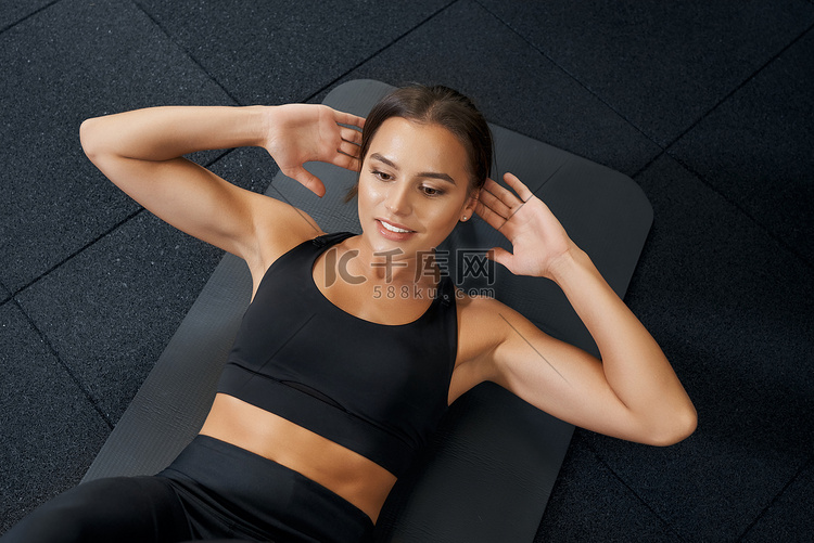 黑发女人在健身房的黑色垫子上做