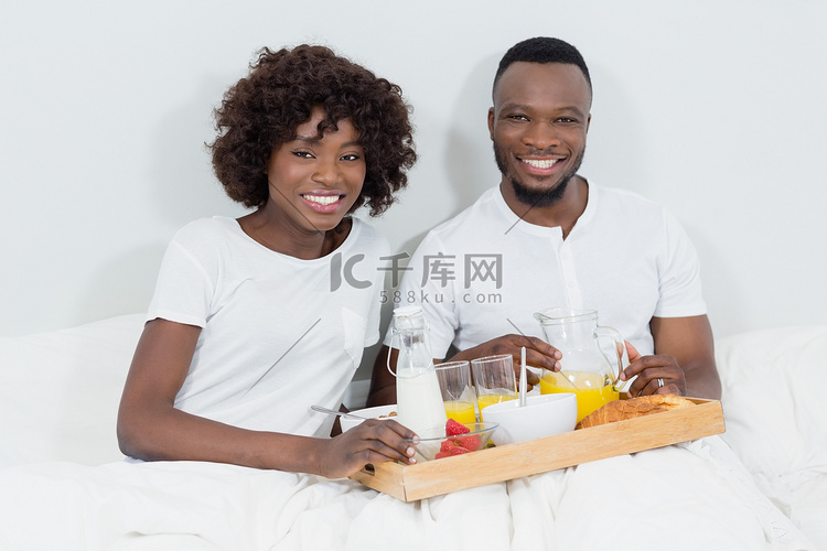 在卧室吃早餐的微笑夫妇的肖像