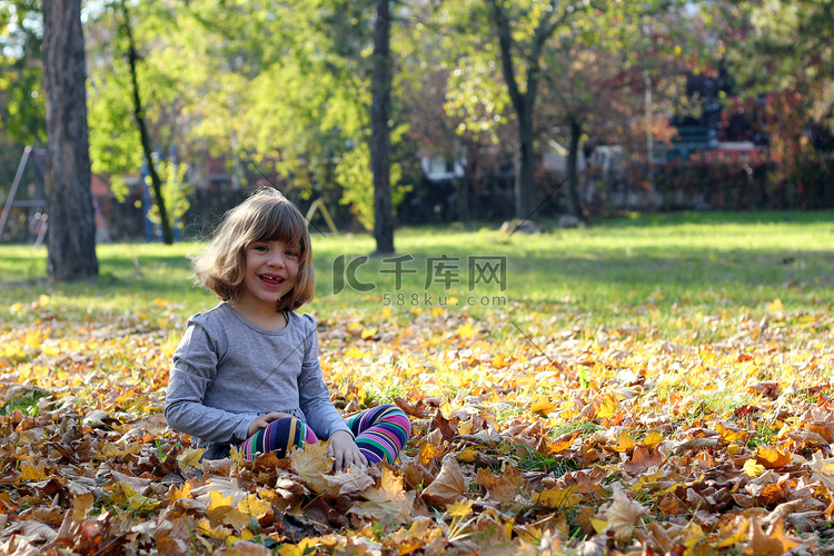秋天公园里坐在树叶上的快乐小女