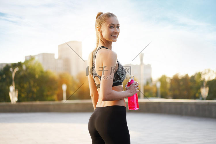 女人在晨练城市背景后喝水红瓶
