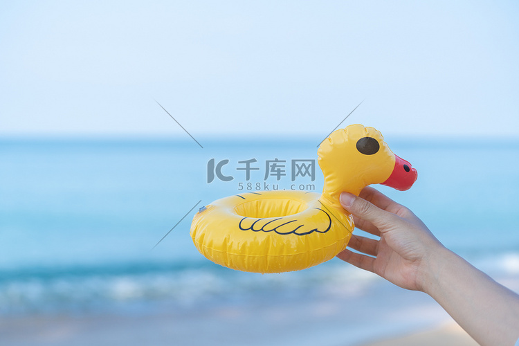 手拿着一只黄色的鸭子在沙滩上，