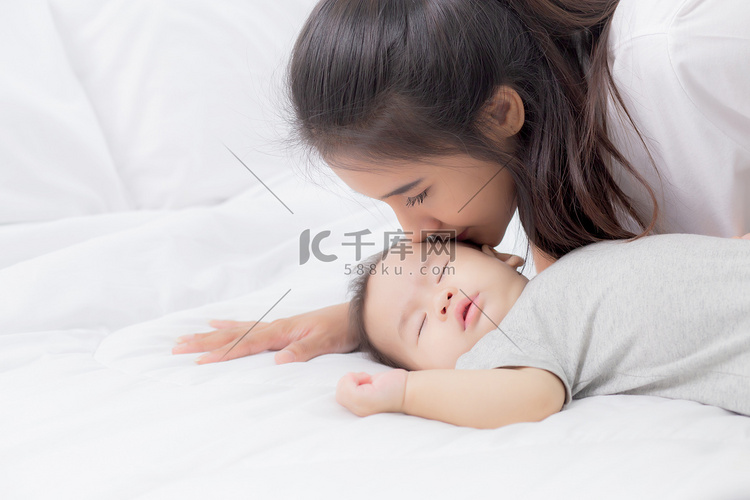年轻的亚洲妈妈在卧室的床上亲吻