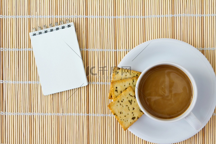 垫子上的白杯热咖啡和白色速写本
