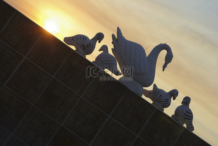 背景为日落的天鹅雕塑剪影。