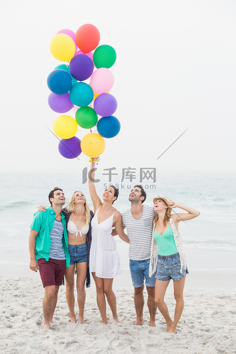 一群朋友拿着气球站在沙滩上