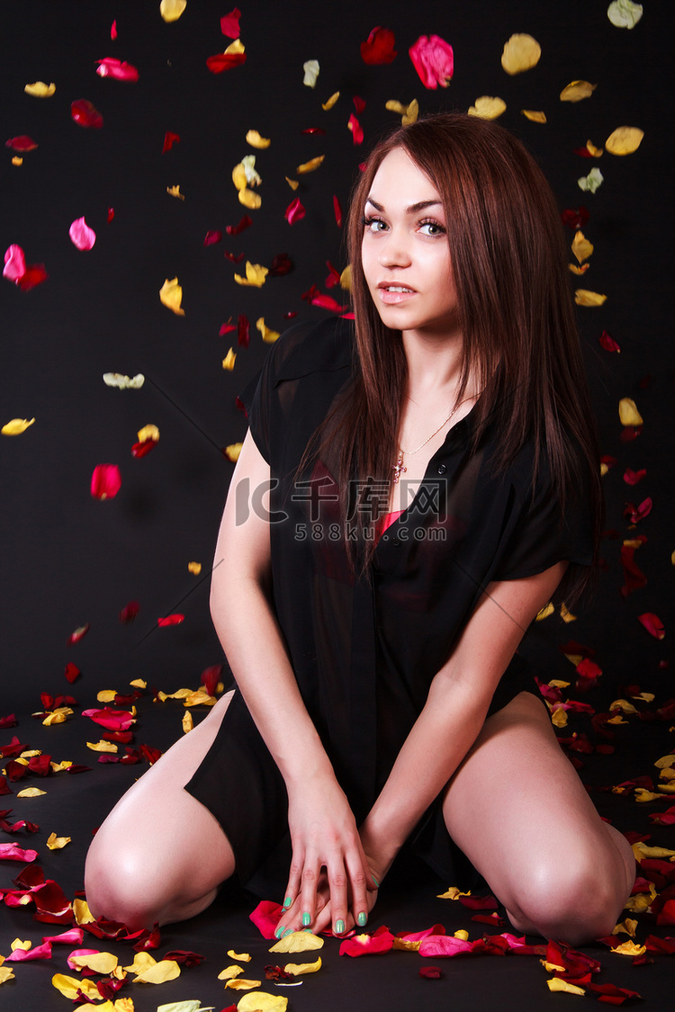 坐在飘落的花瓣下的美丽的年轻女